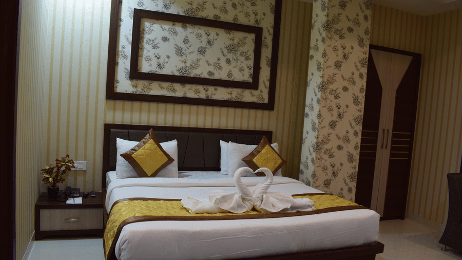A spacious room with a bed decorated with towel swans and a wooden bedside table at Hotel Uday Palace.