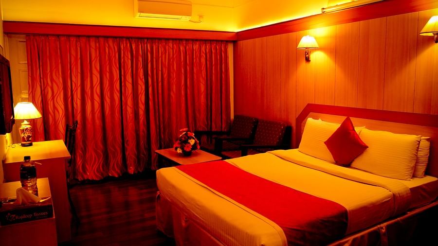  Hotel Yasodha Towers - Interior view of a bedroom with a king size bed with a red throw pillow, red curtains and wooden flooring