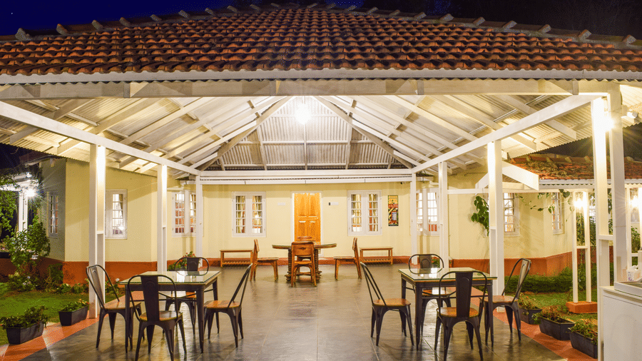 Open air dining pavilion at Ibex Resort Coonoor with tiled roof wooden beams and neatly arranged tables offering a relaxed alfresco dining experience surrounded by the scenic beauty of the hills.
