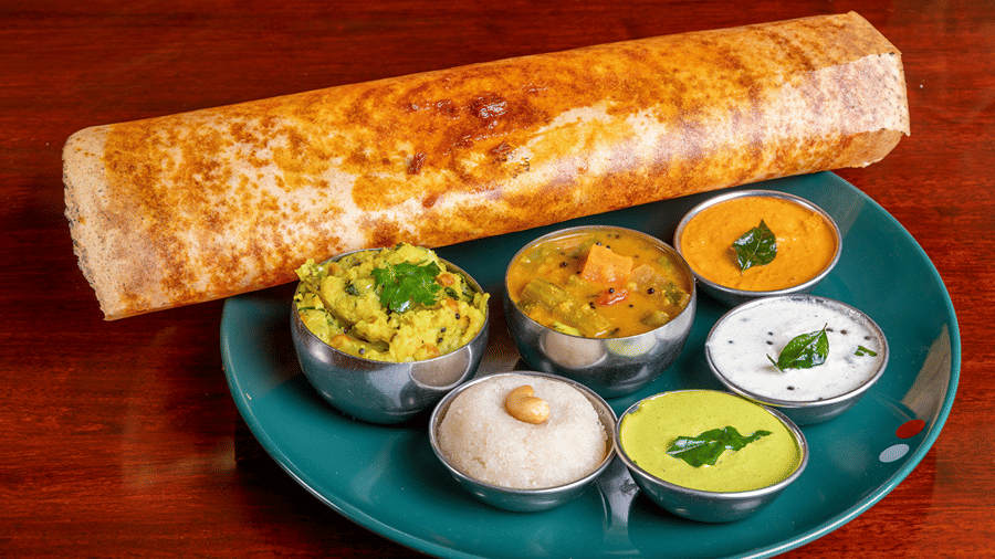 A crispy dosa with many dips of chutney and sambar with kesaribath, served on a plate.