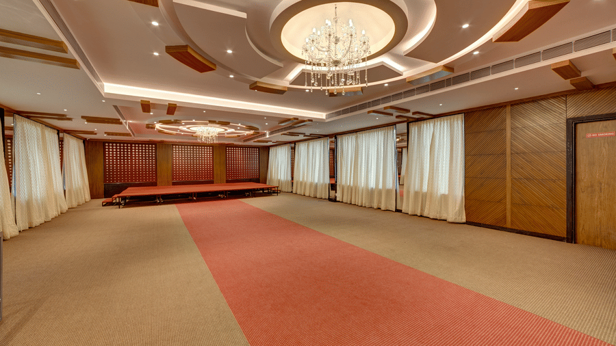 A large banquet hall with a red carpet in the centre, a decorative chandelier, and wooden walls at Icon Express By Bhagini, Mahadevapura.
