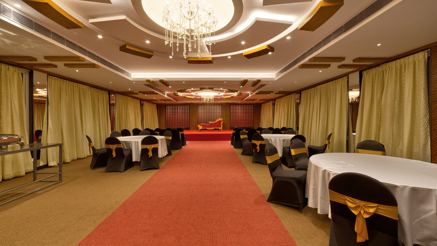 A red carpet, a decorative chandelier, and round tables with white cloths in the banquet hall at Icon Express By Bhagini, Mahadevapura.
