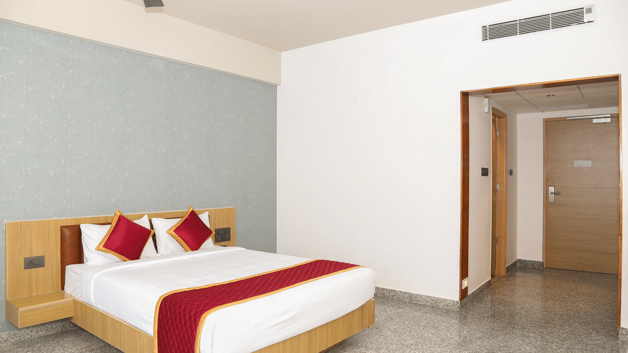 A double bed with a red runner, white walls, and an open wooden door at Icon Express By Bhagini, Mahadevapura.
