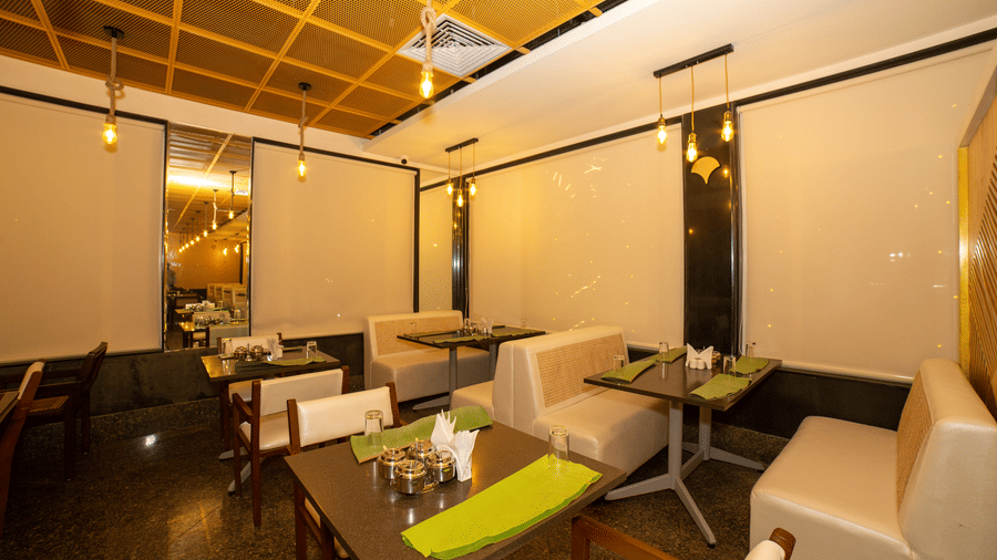 Close view of dining tables, chairs, and green placemats under a wooden trellis ceiling in the restaurant of Icon Express By Bhagini, Mahadevapura.