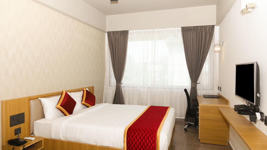 A double bed, a window with curtains, and a wall-mounted television at Icon Express By Bhagini, Mahadevapura.