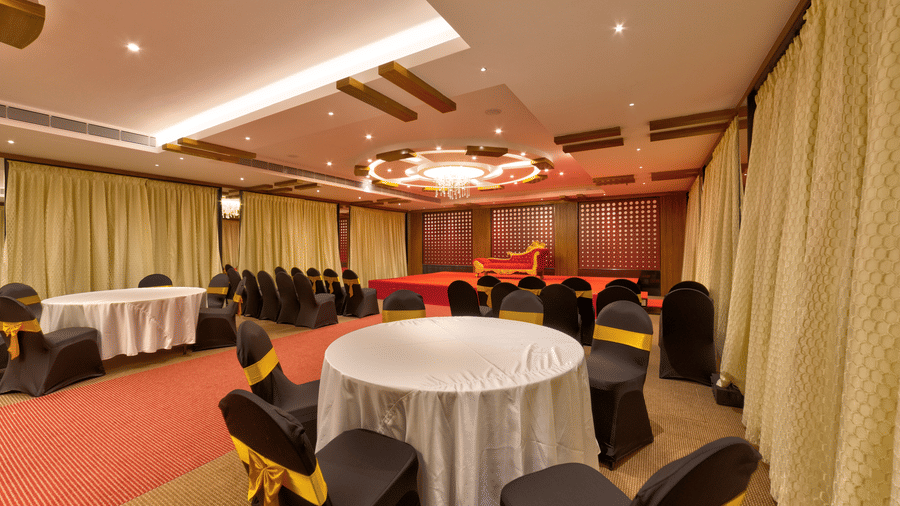 Round tables, black and gold chairs, a red carpet, and a stage setup inside the banquet hall of Icon Express By Bhagini, Mahadevapura.