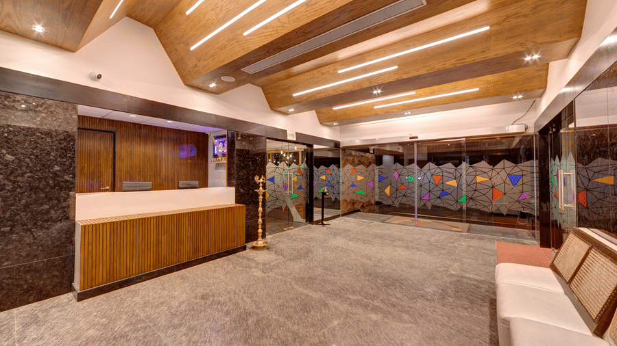 A wooden reception desk, white seating, and a wooden slatted ceiling in the lobby of Icon Express By Bhagini, Mahadevapura.