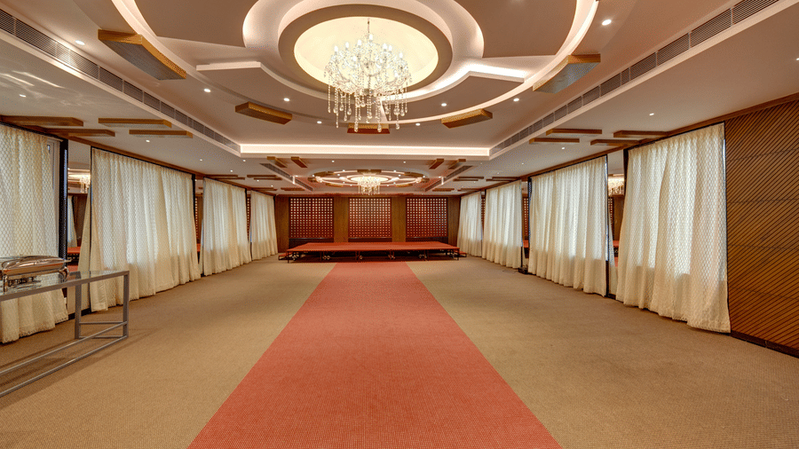 A spacious banquet hall with a red carpet in the centre, a decorative chandelier, and wooden walls at Icon Express By Bhagini, Mahadevapura.