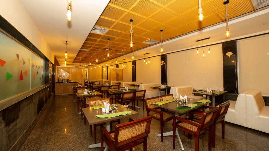 Wide view of the main dining hall, showing arranged tables, chairs, white booths, and a decorative ceiling at Icon Express By Bhagini, Mahadevapura.