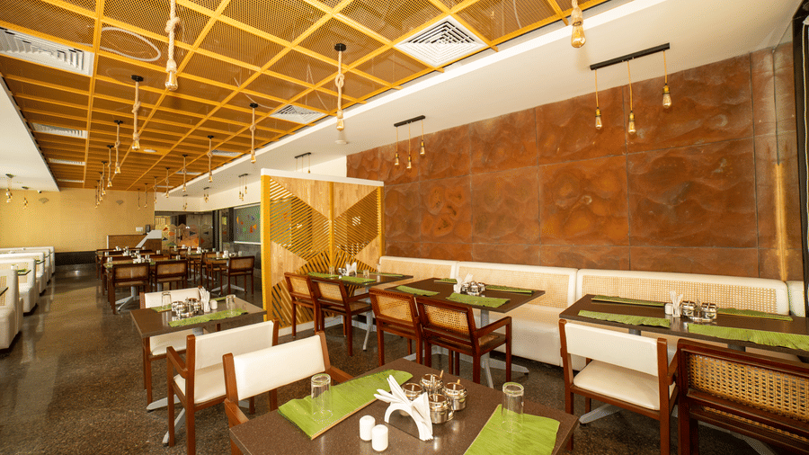 Arranged tables, wooden chairs, green placemats, and a textured brown wall in the dining centre at Icon Express By Bhagini, Mahadevapura.