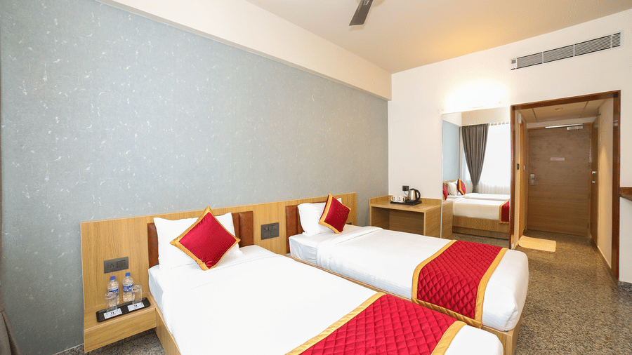 Two single beds with red runners, white linens, and a central bedside table at Icon Express By Bhagini, Mahadevapura.