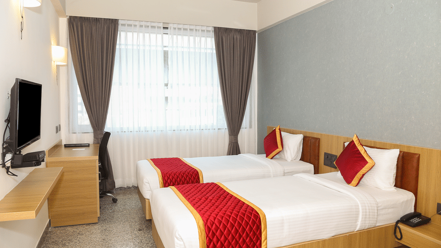 Two single beds, a window with curtains, and a wooden desk at Icon Express By Bhagini, Mahadevapura.
