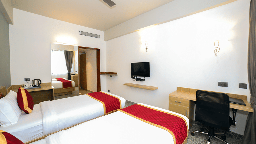 Two single beds, a wall-mounted television, and a desk with a chair at Icon Express By Bhagini, Mahadevapura.