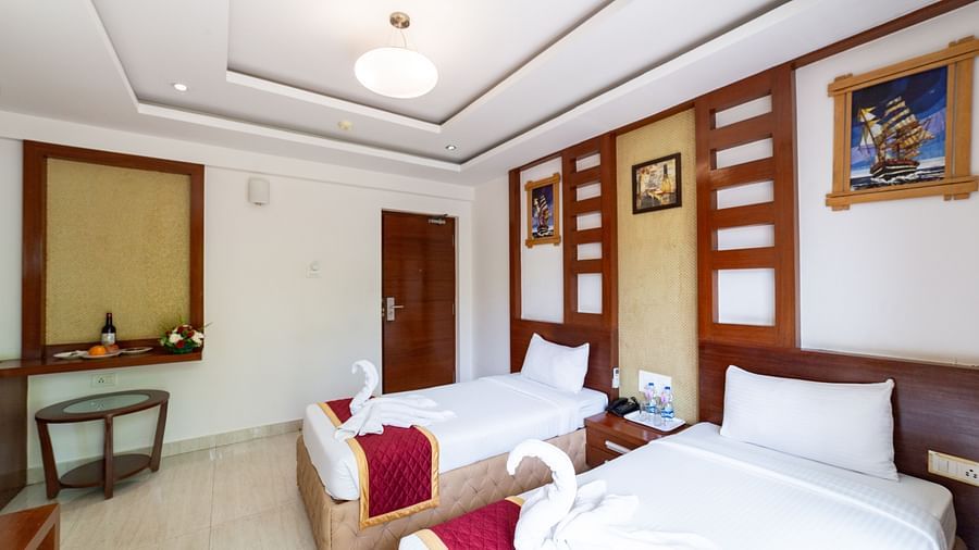 Symmetrically designed Deluxe Twin Room with a soft false ceiling light, decorative wall panels, and plush bedding—ideal for dual occupancy with ample walking space.