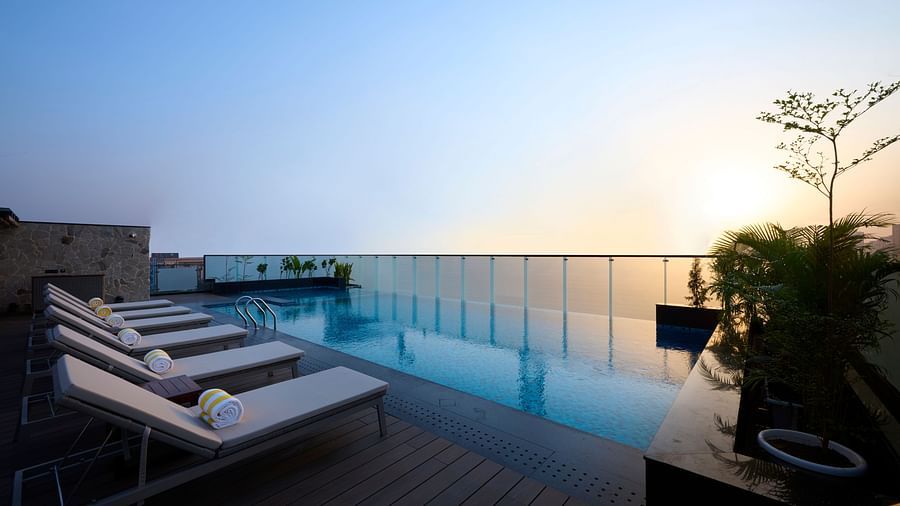 A rooftop pool offers a tranquil setting with lounge chairs lined up beside the water, under a clear sky transitioning from day to evening. - Iris Sarovar Portico, Sector 85, Gurugram