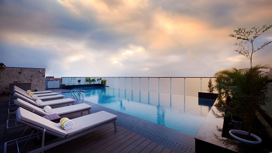 A rooftop swimming pool reflects the colours of the evening sky, with lounge chairs arranged along the side, inviting relaxation by the water. - Iris Sarovar Portico, Sector 85, Gurugram
