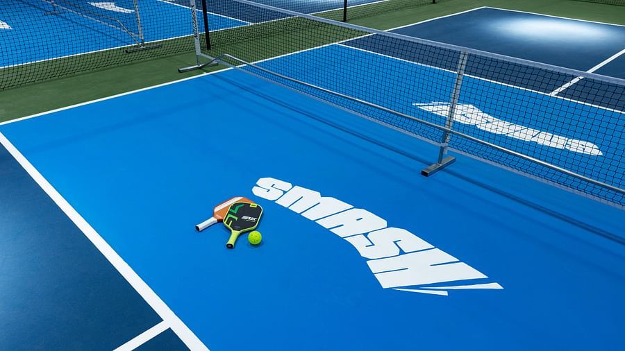 Close-up view of indoor pickleball courts with paddles and balls placed on a blue surface marked 'SMASH,' at Jenneys Residency, Coimbatore.