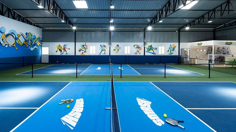 Indoor pickleball courts with paddles and balls on blue surfaces, located at Jenneys Residency, Coimbatore.