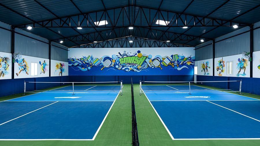 Symmetrical view of multiple indoor pickleball courts with blue and green flooring and colourful wall art, at Jenneys Residency, Coimbatore.