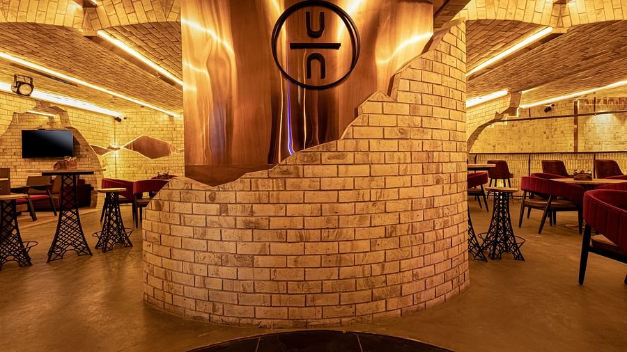 The Underground Bar restaurant interior with warm lighting, brick walls, and a large copper feature displaying a logo. Tables and chairs are neatly arranged