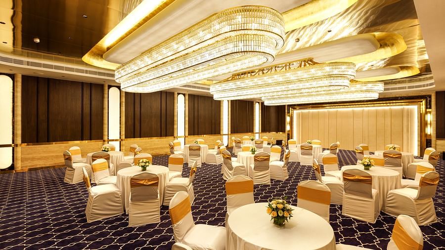 Luxurious banquet hall set up with round tables and white chairs with gold sashes, under elegant chandeliers, at Jenneys Residency, Coimbatore.