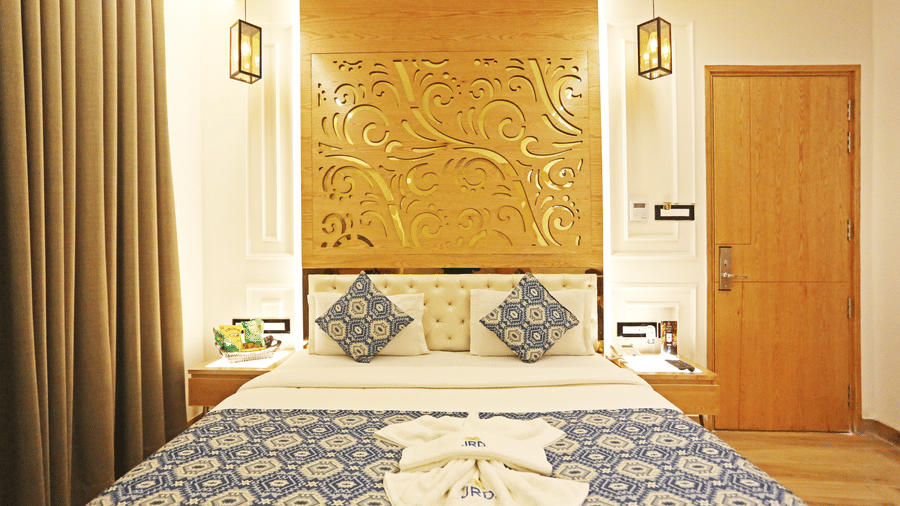 A bedroom featuring a neatly-made bed with blue-patterned cushions and an ornate wooden headboard at JRD Luxury - Business Hotel.