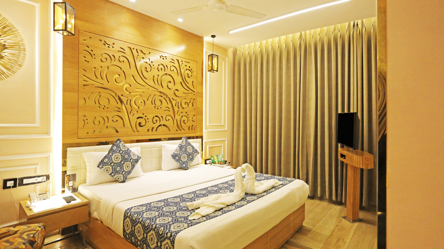 The Deluxe Room of JRD Luxury Business Hotel showcasing a double bed, wooden flooring, a television,  and ceiling lights.