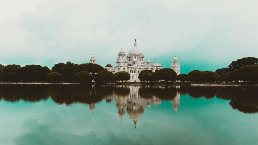 A white dome like building with trees surrounding it and their reflection on a water body.