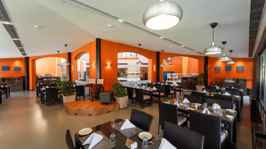 Bright restaurant hall with warm orange accent walls and elegant pendant lighting at Kenilworth Resort & Spa, Goa.