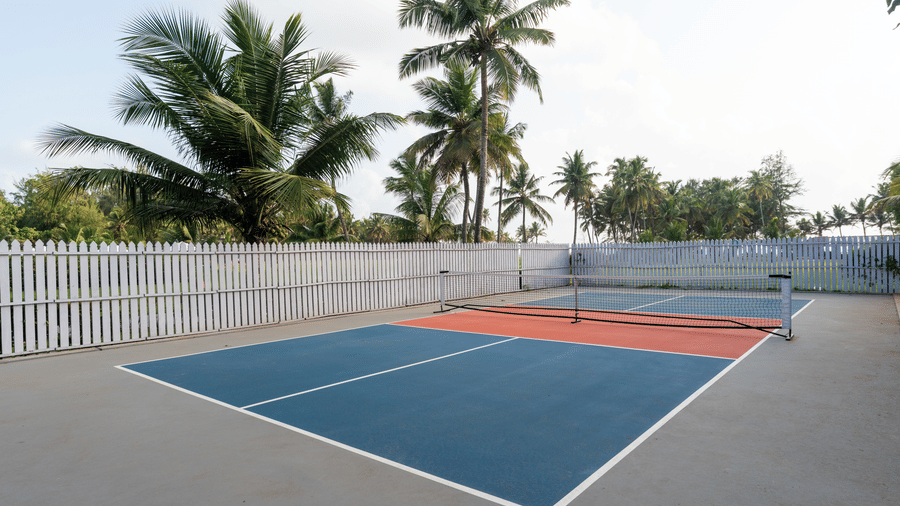 Outdoor pickleball court surrounded by palm trees and white fencing at Kenilworth Resort & Spa, Goa.