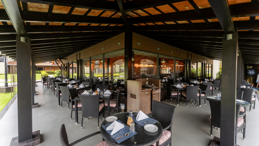 Shaded outdoor dining patio with tables and chairs at Kenilworth Resort & Spa, Goa.