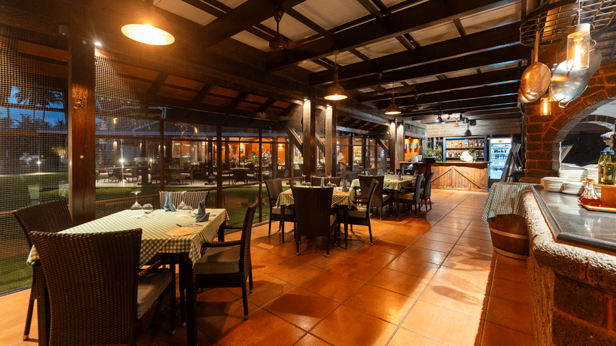 Warmly lit open-air restaurant with dark dining tables at Kenilworth Resort & Spa, Goa.