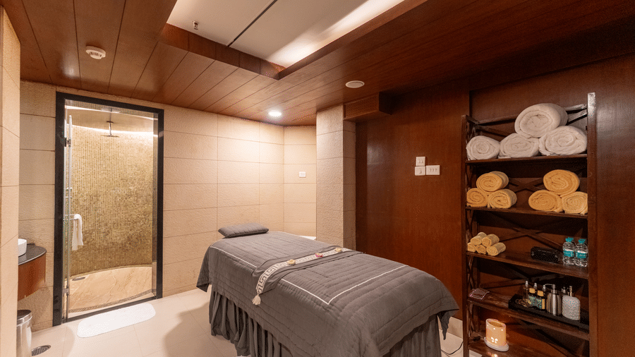 Warmly lit single spa therapy room with massage table and glass shower stall at Kenilworth Resort & Spa, Goa.