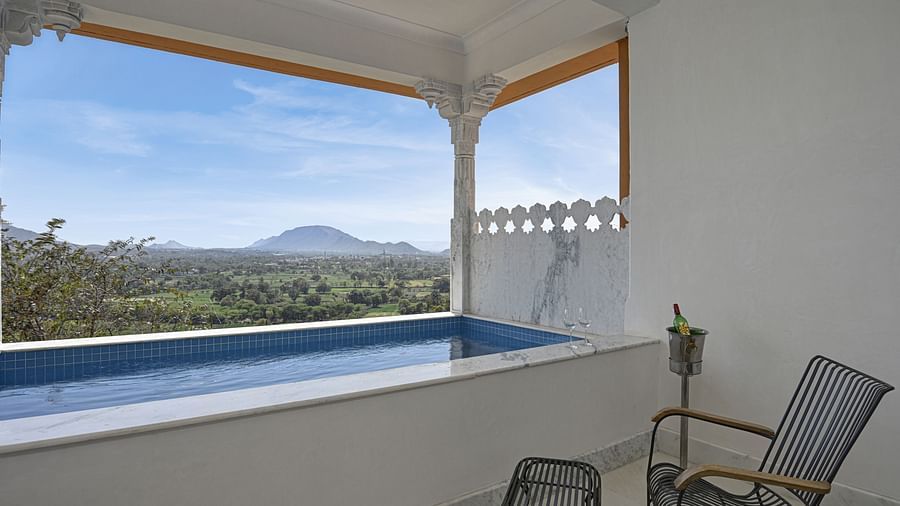 Shot of a view from a balcony of Plunge Pool Suite at Khas Mahal by Fateh Collection, Udaipur with a pool, overlooking a green landscape and mountains under a blue sky.