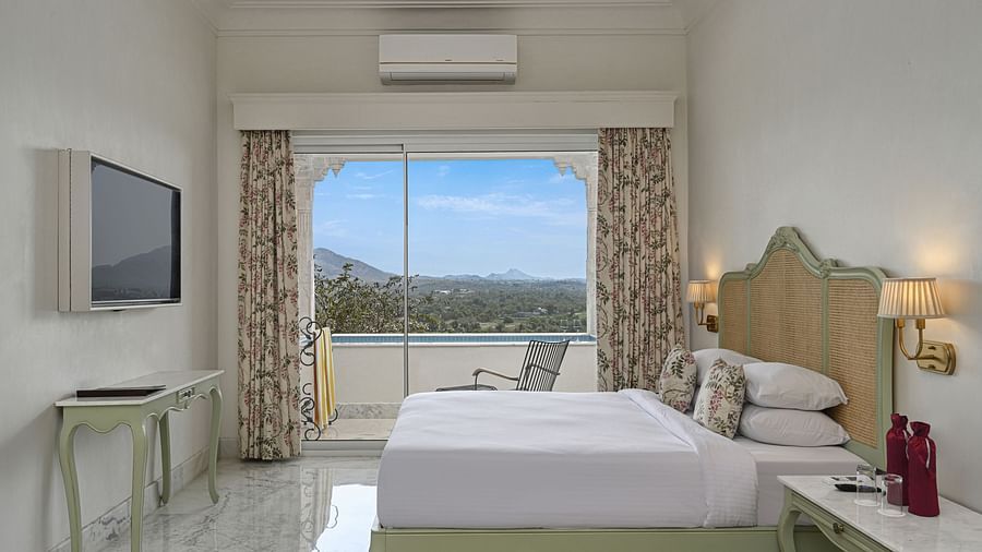 Side view of a  well-lit Plunge Pool Suite at Khas Mahal by Fateh Collection, Udaipur featuring a bed, seating area, and a large window with a view.
