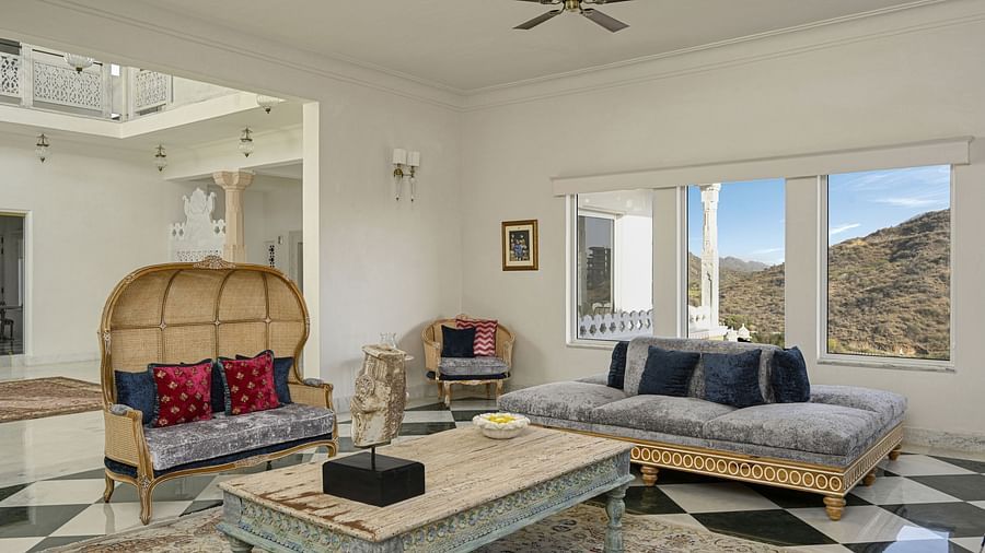 A bright, modern living room featuring a wicker peacock chair with colourful cushions, a light-colored coffee table, and a daybed by the window at Khas Mahal by Fateh Collection, Udaipur.