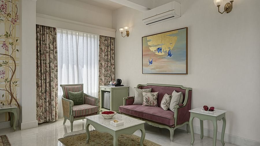 A well decorated corner of Heritage Chamber Suite at Khas Mahal by Fateh Collection, Udaipur features a sofa with decorative pillows, an armchair, a coffee table, and a side table.