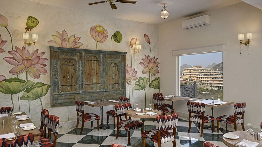 A brightly lit restaurant interior with a black and white checkered floor, floral-themed wall art, and dark wood furniture at Khas Mahal by Fateh Collection, Udaipur.
