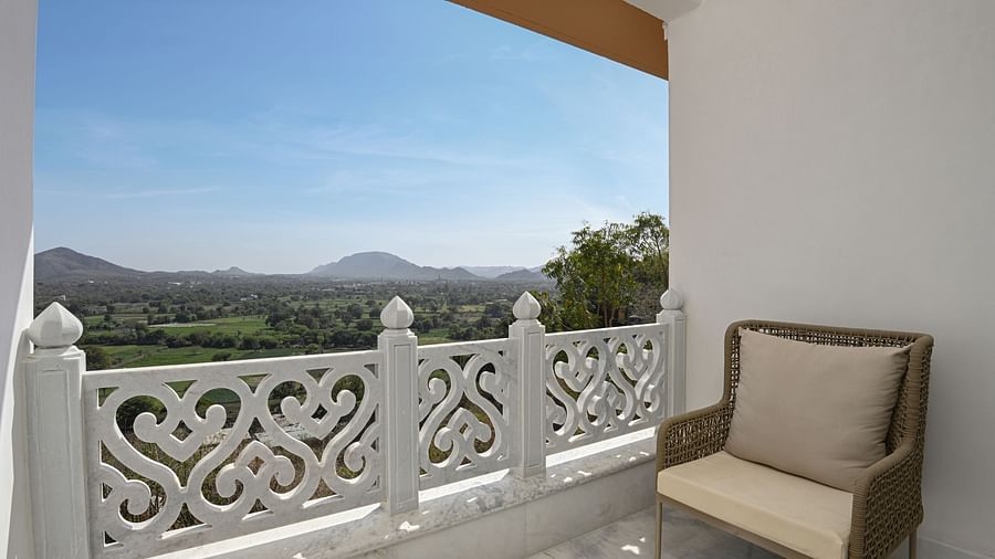 A balcony of Heritage Chamber Suite at Khas Mahal by Fateh Collection, Udaipur with a chair overlooking a view of mountains.