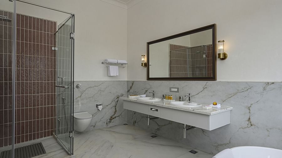 A well-lit, modern bathroom featuring a shower with a dark-tiled interior, a long, white double sink vanity, and a rectangular mirror with black trim at Heritage Chamber Suite at Khas Mahal by Fateh Collection, Udaipur.