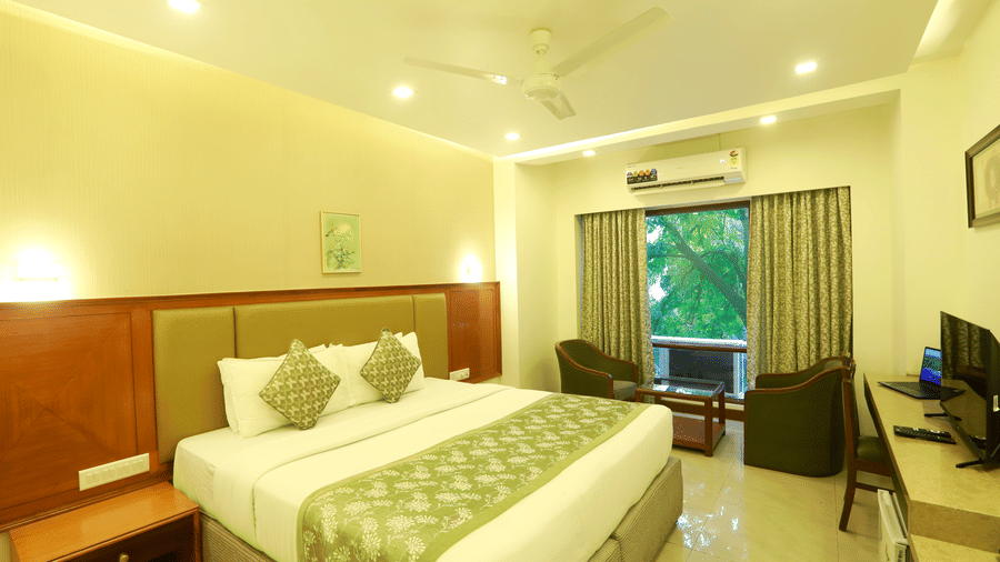 The Deluxe Room at Kohinoor Executive featuring a double bed, seating area, and warm lighting.