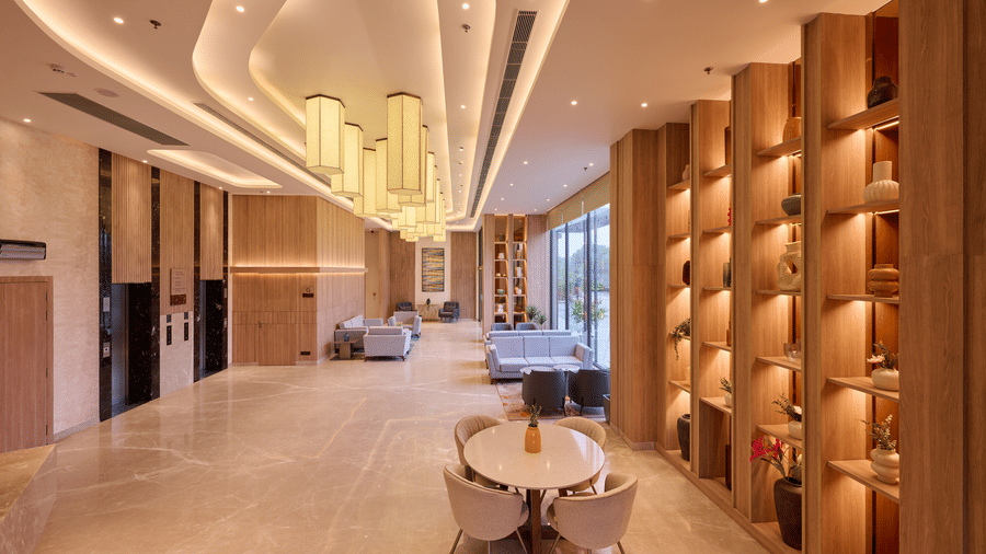 A hotel lobby at KPG Sarovar Portico, Raj Nagar Extension, Ghaziabad featuring a round table with chairs, display shelves, ceiling lights, and sofa seating.