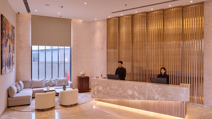 A reception desk at KPG Sarovar Portico, Raj Nagar Extension, Ghaziabad featuring 2 receptionists, computer monitors, a front counter, and a sofa seating area.