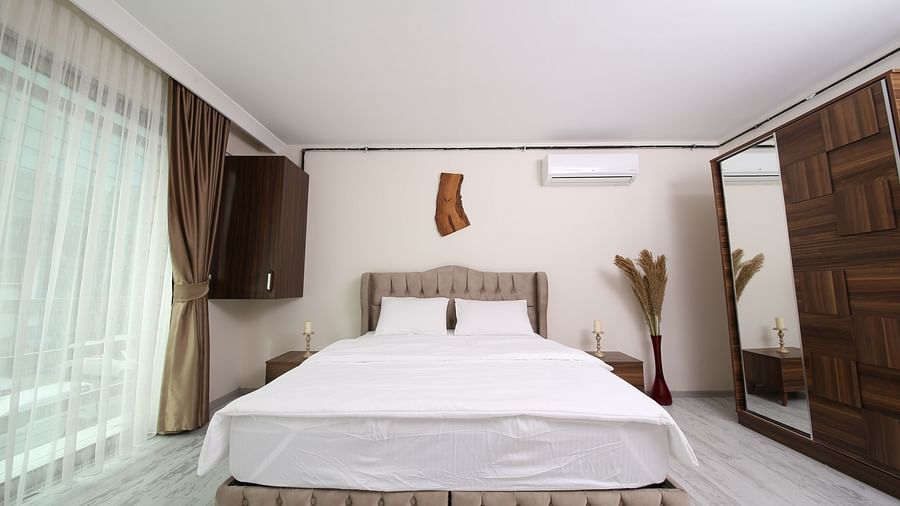 Wide view of a double bed with white bedsheet and two pillows and a wooden cupboard beside it
