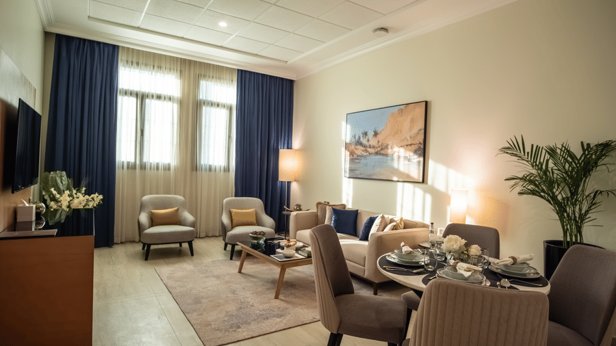 Living/dining area. Beige sofa, grey armchairs, set dining table, and a large landscape painting on a neutral wall.