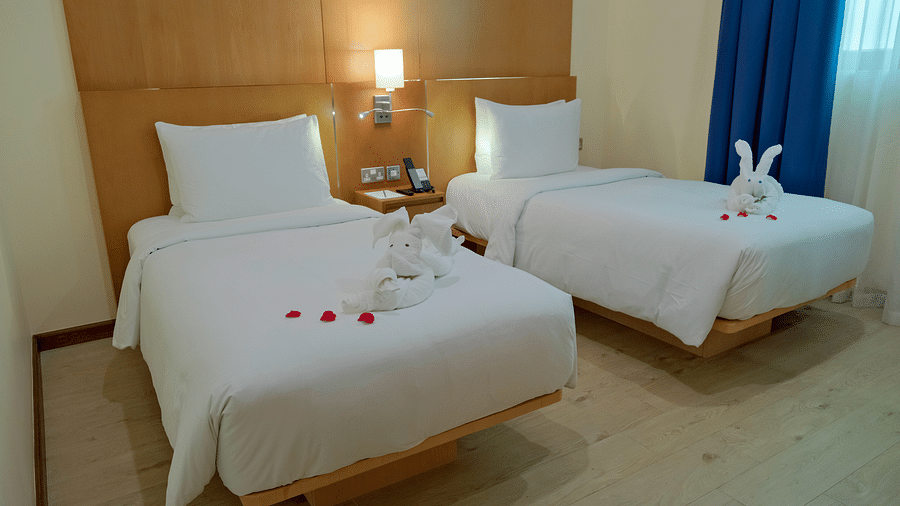 Close-up corner view of a deluxe two-bedroom apartment featuring twin beds, a bedside table with a light, and a towel-folded rabbit on the bed.