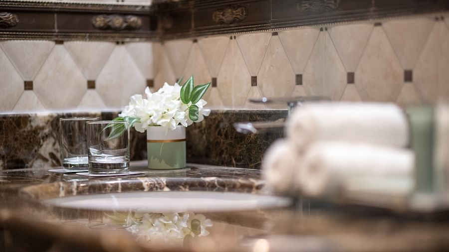 close up shot of a wash basin inside a bathroom with towels and a small vase - La Maison Hotel, Doha