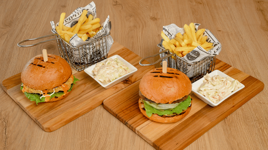 Two burgers with golden chips and creamy dips presented on wooden boards at La Maison Hotel, Doha.