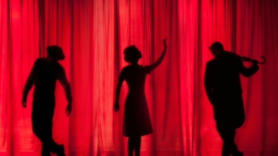 three people on the stage performing in a theatre with red curtains in the background