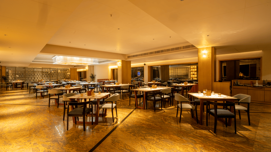 The Wild Fork restaurant at La Marvella, Bengaluru featuring several sets of table and chairs and a shelve where several liquor bottles are kept.